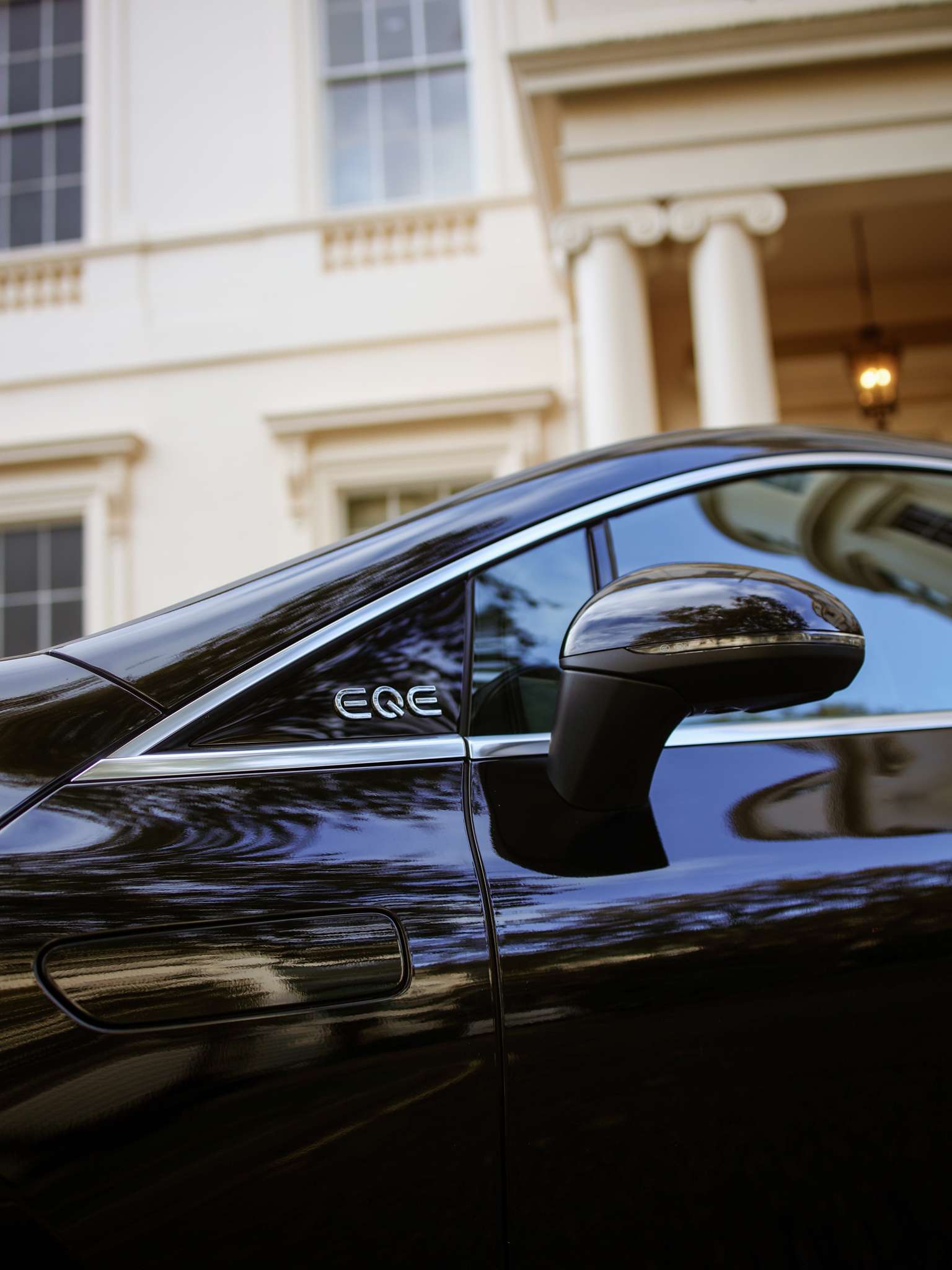 New-Dawn-Of Luxury-Section/Mercedes-EQE-Page A black car parked in front of a large building, showcasing the vehicle's sleek design against the architectural backdrop