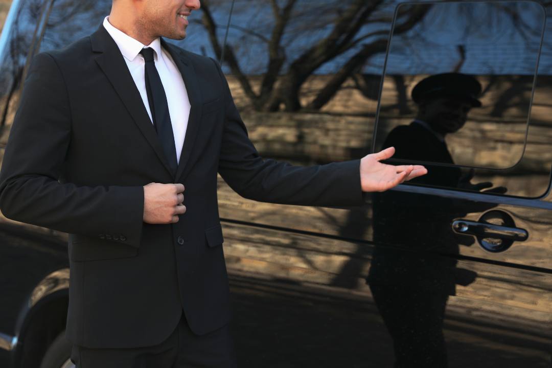 A man in a suit and tie stands beside a sleek black car, exuding professionalism and confidence