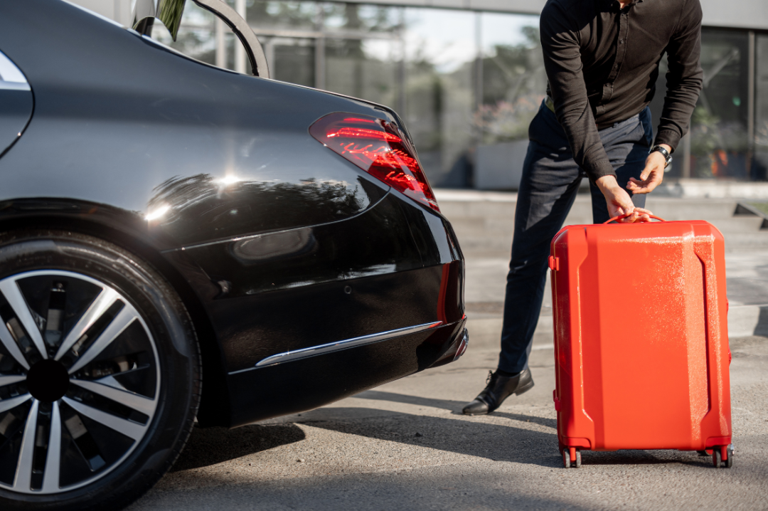 A man stands beside a car, holding a suitcase, ready for travel