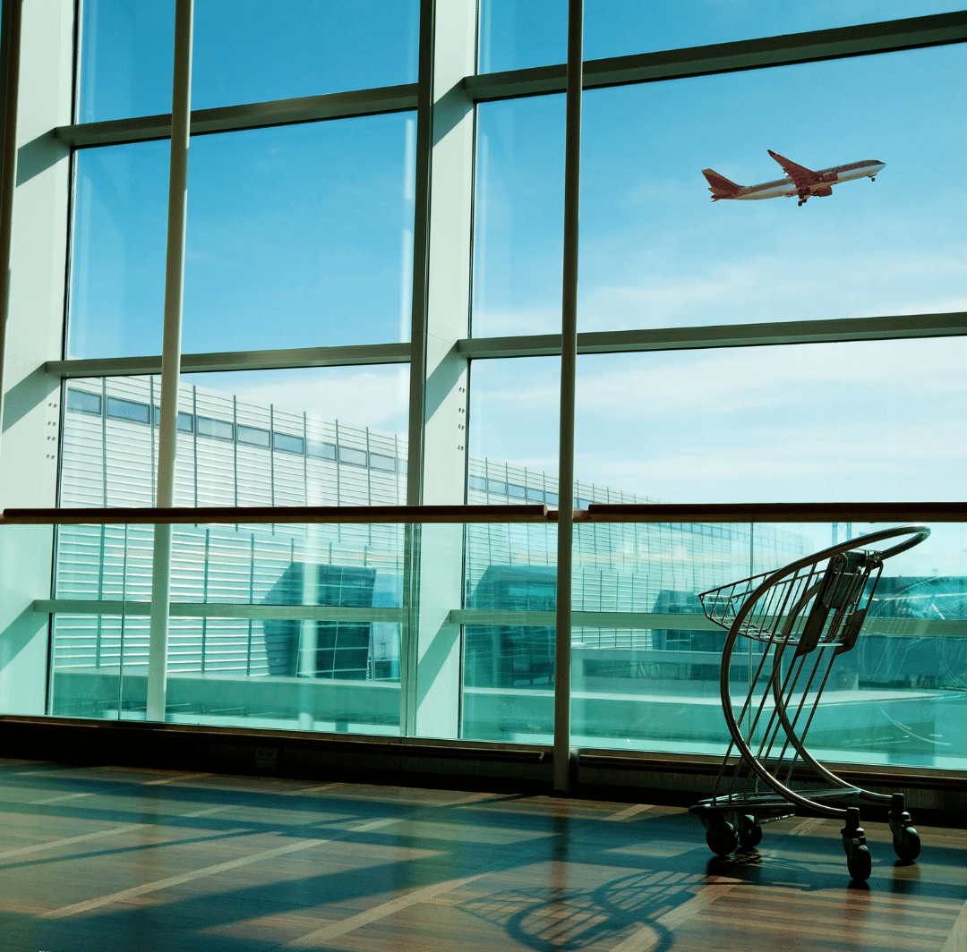 A plane is captured in flight above a large window at the airport, providing a glimpse of the terminal setting