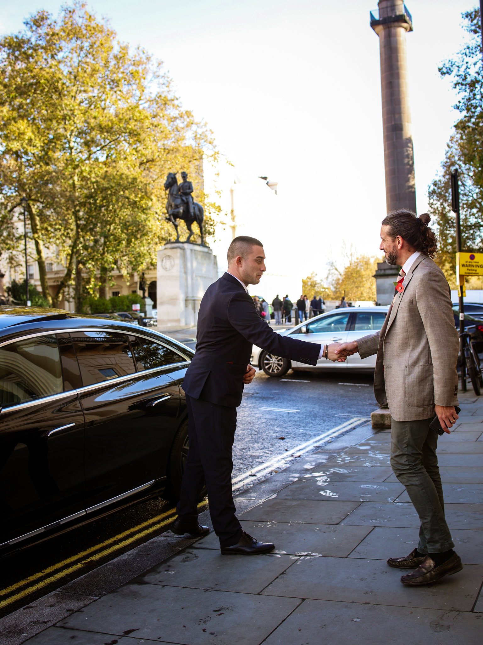 A handshake between two men occurs on a sidewalk, symbolizing agreement or a successful meeting